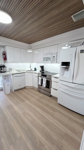 A modern kitchen with white cabinetry, stainless steel appliances, and a wooden ceiling. - Entire House Climatized Pool Close to the Beach (Hollywood)