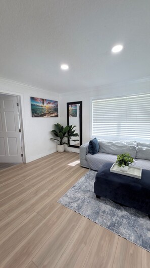 A modern living room with a grey sofa, a coffee table with a plant, a large mirror, and a painting on the wall.