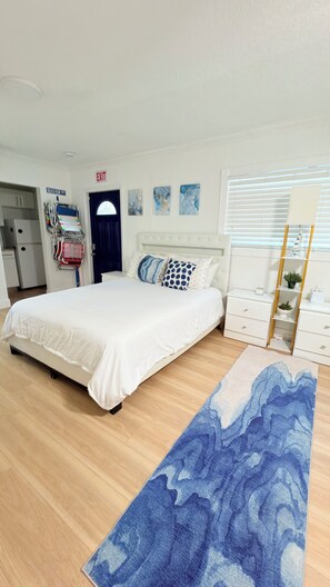 A hotel room with a bed, a desk, a chair, a window with blinds, and a door marked 'EXIT'.