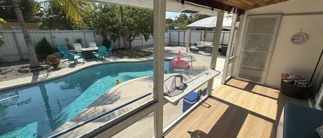 A covered outdoor area with a pool, a table, chairs, and a wicker basket.