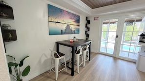 A dining area with a table and chairs, a painting of birds, and an exit sign. - Entire House Climatized Pool Close to the Beach (Hollywood)