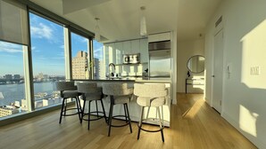 A modern kitchen with a large window, a bar area with stools, and a view of a river and cityscape. - 2 bed/2 bath luxe condo in Midtown  (New York)