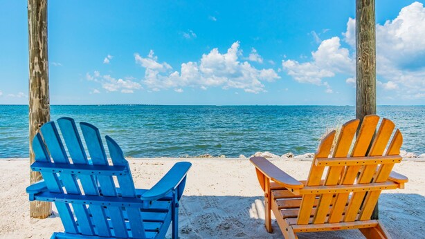 Dos sillas Adirondack sobre una playa arenosa con vista al océano.