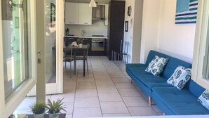 An open-plan living area with a sofa, dining table, chairs, and a kitchen in the background. - MDS 3 - My Home in Como (Muronico)