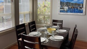A dining area with a table set for four, four chairs, a chandelier, and a painting of a harbor scene.