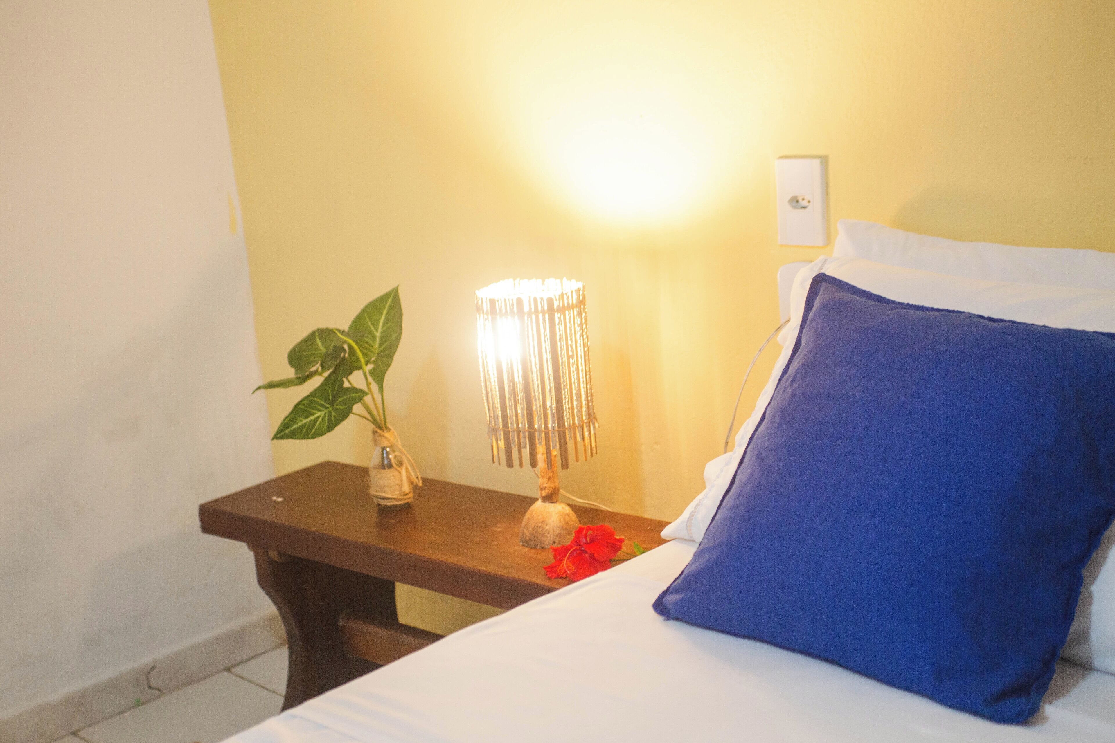 Una cama con un cojín azul, una mesita de noche con una lámpara y una planta en maceta.