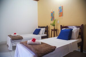 Habitación de hotel con dos camas individuales, cada una con una manta marr ón y una flor roja. Hay dos cuadros en la pared y una pequeña planta en maceta sobre una mesita.