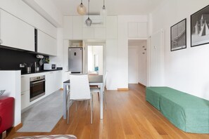 A modern kitchen with white cabinetry, a dining area with a white table and chairs, and a green bench.