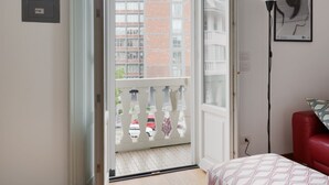 A room with a bed, a red chair, a white lamp, and a balcony with a view of buildings. - GuestHost - Buschi Milano-Città Studi Apartment (Milano)