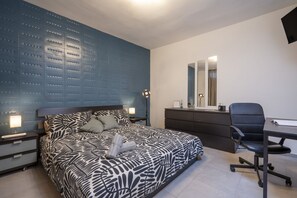 A bedroom with a bed, bedside tables, a desk, a chair, and a dresser.
