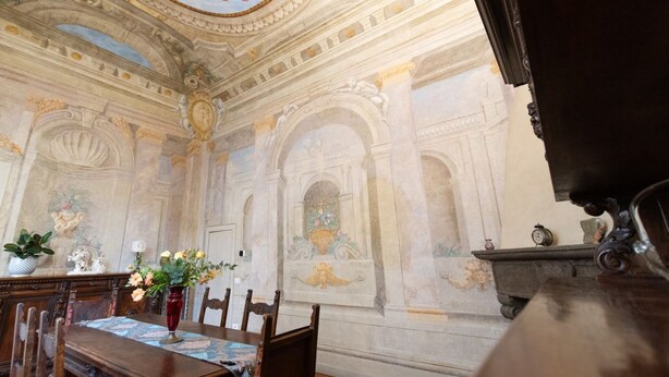 An ornate room with a high ceiling, detailed frescoes, a wooden table with chairs, and a vase with flowers. - Santo Spirito Frescoed 6 sleeps apartment (Firenze)