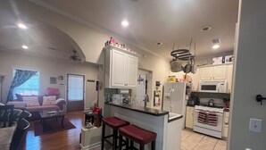 A kitchen with white cabinets, a central island with stools, a microwave, stove, and a refrigerator. - Lovely home in good location just few minutes to OleMiss and downtown.  (Oxford)