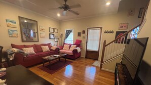 A living room with a red sofa, a coffee table, wooden flooring, a ceiling fan, and a staircase leading to another level. - Lovely home in good location just few minutes to OleMiss and downtown.  (Oxford)