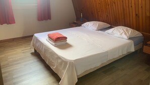 Un dormitorio con techo de madera, una cama con ropa de cama blanca y un ventanal con cortinas.
