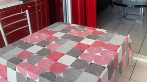 Cocina compacta con microondas, horno y armarios rojos. En primer plano, una mesa con mantel estampado geométricamente.