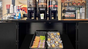 A coffee station with three coffee makers labeled 'dark roast' and 'light roast', a coffee dispenser, and a tray of assorted pastries. -  Relax Suites Extended Stay - La Mirada (La Mirada)