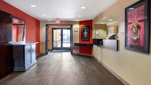 A hotel corridor with red walls, an exit sign, a reception desk, and framed artwork on the walls. -  Relax Suites Extended Stay - La Mirada (La Mirada)