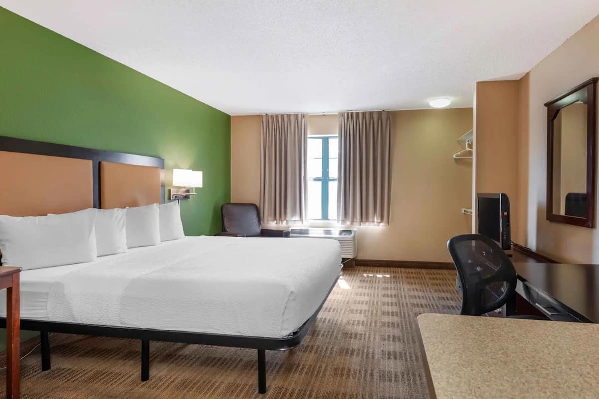 Une chambre d’hôtel avec un grand lit, un bureau, une chaise, un appareil de climatisation et un téléviseur.
