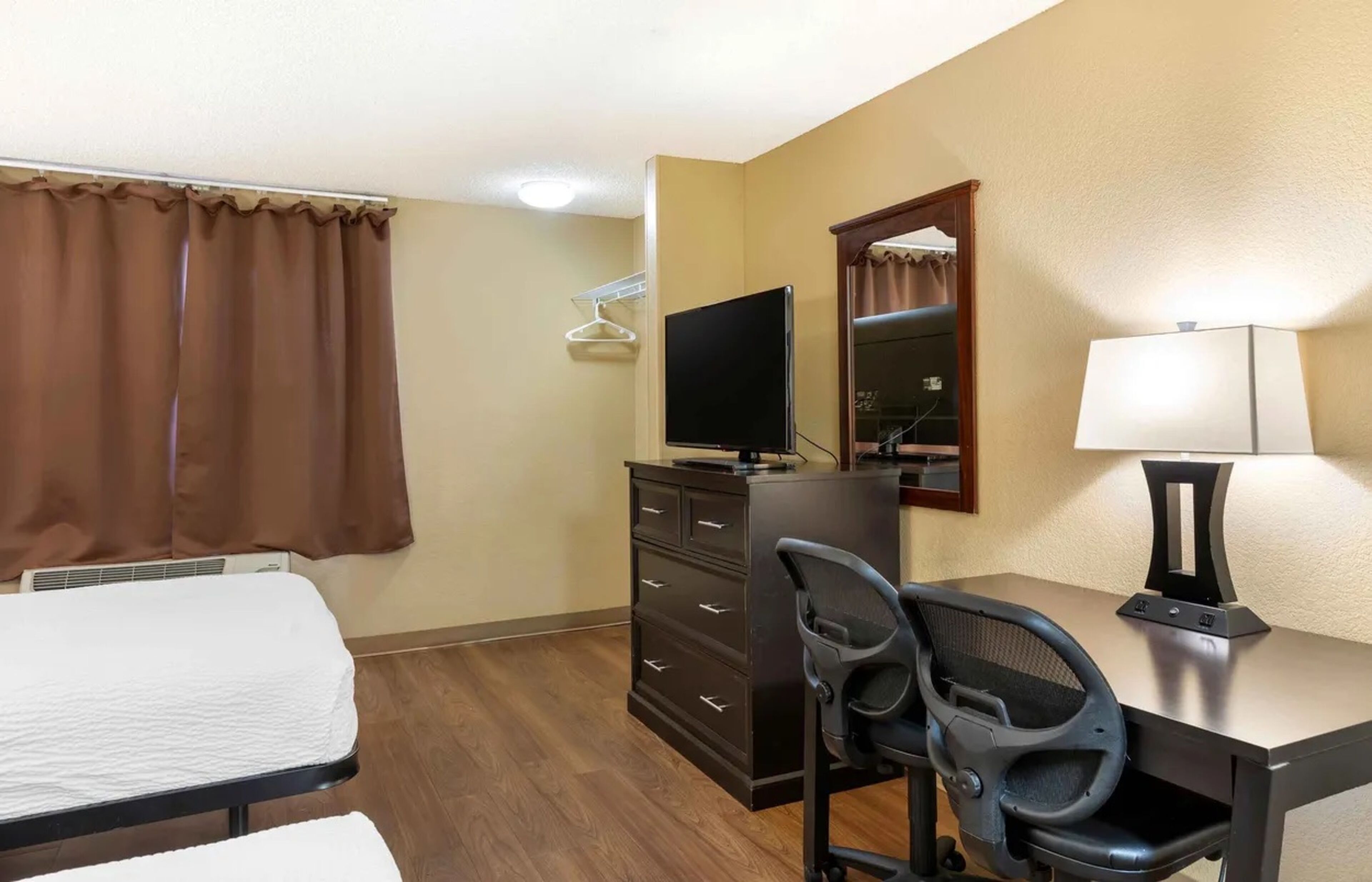 A hotel room with a bed, a desk with a chair, a television, a dresser, and a lamp.