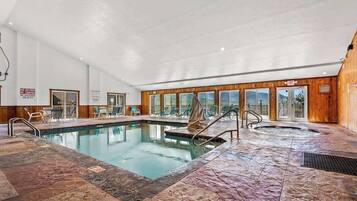 Una piscina interna con idromassaggio, sedie a sdraio e vista sull'esterno.