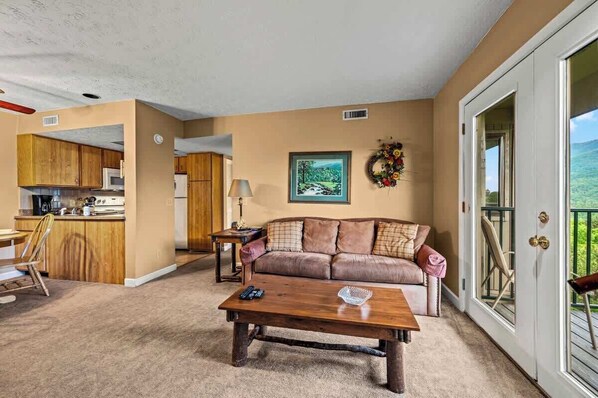A living room with a sofa, coffee table, and a view of a kitchen and balcony.