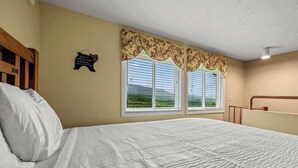Un dormitorio con una cama grande, dos ventanas con persianas, un cabecero de madera y un letrero en la pared.
