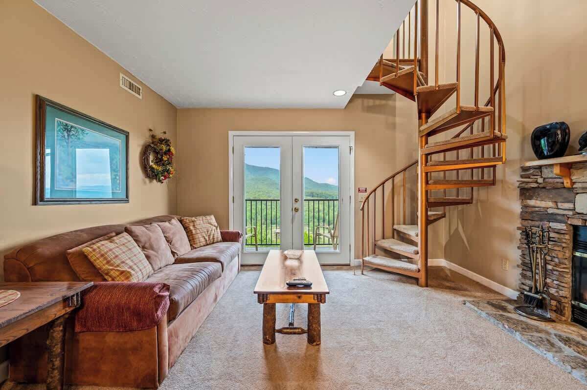 A living room with a brown leather sofa, a wooden coffee table, a spiral staircase, and a stone fireplace.
