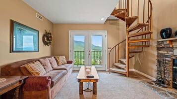 A living room with a brown leather sofa, a wooden coffee table, a spiral staircase, and a stone fireplace.