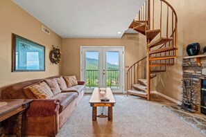 A living room with a brown leather sofa, a wooden coffee table, a spiral staircase, and a stone fireplace.