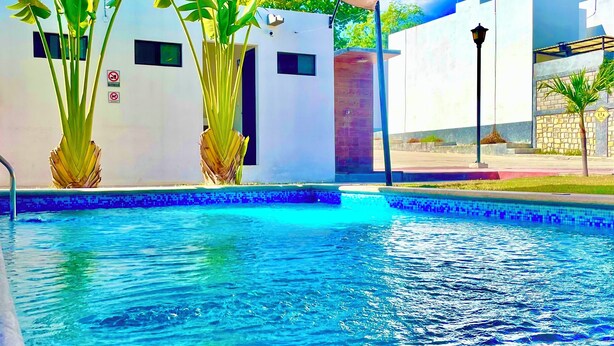 A swimming pool with clear blue water, surrounded by white walls and potted plants. - Oferta Excelente Casa En Residencial Privada, Alberca, Asador (Ciudad Valles)