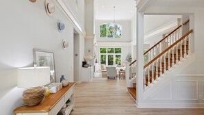A spacious hallway with a wooden floor, a staircase with white railings, and a large window providing natural light.