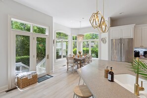 A spacious kitchen with a large island, white cabinetry, and a view of a lush garden.