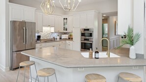 A modern kitchen with white cabinetry, stainless steel appliances, a central island with stools, and decorative lighting.