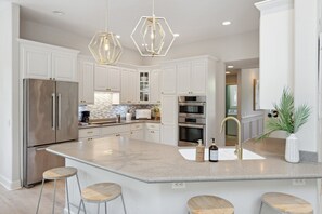 Una cucina moderna con mobili bianchi, elettrodomestici in acciaio inossidabile, un'isola centrale con sgabelli e illuminazione decorativa.