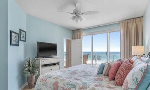 A bedroom with a bed, a television, a plant, and a view of the ocean.