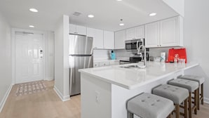 A modern kitchen with white cabinets, stainless steel appliances, and a central island with bar stools. - BEACHFRONT CONDO, FAMILY FRIENDLY, LOW FLOOR, OUTDOOR POOL (Gulf Shores)