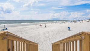 A beach with a wooden walkway leading to the water, sandy beach, and umbrellas. - BEACHFRONT CONDO, FAMILY FRIENDLY, LOW FLOOR, OUTDOOR POOL (Gulf Shores)