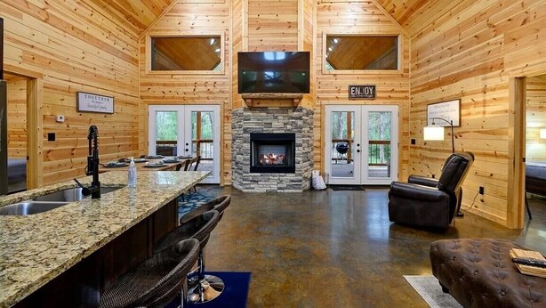 A log cabin interior with a stone fireplace, a kitchen area, and a seating area with a fireplace. - Crystal Moon - Hot Tub, Firepit, Cornhole, Hammock (Broken Bow)