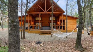A wooden cabin with a large porch, surrounded by trees. - Crystal Moon - Hot Tub, Firepit, Cornhole, Hammock (Broken Bow)