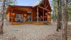 A wooden cabin with a covered porch and a deck, surrounded by trees. - Crystal Moon - Hot Tub, Firepit, Cornhole, Hammock (Broken Bow)