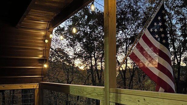 A wooden deck with a railing, a table, and chairs, and an American flag.