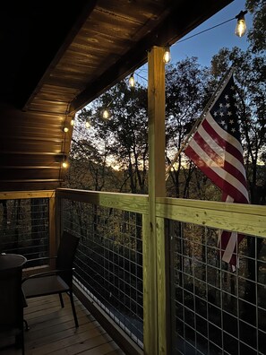 A wooden deck with a railing, a table, and chairs, and an American flag.