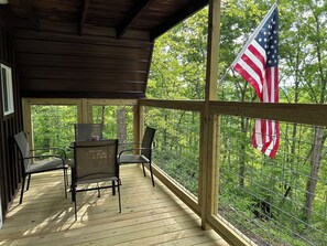 A wooden deck with chairs and a table, surrounded by a metal fence and a view of trees.