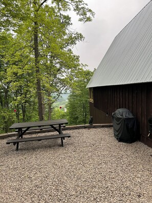 A picnic table and an owl statue in a gravel area with a barn and trees in the background.