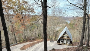 A cabin with a triangular roof, surrounded by a forested area with a dirt path leading to it.