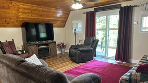 A cozy living room with a wooden ceiling, a flat-screen TV, a fireplace, and a comfortable seating area.