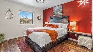 A bedroom with a large bed, a window, a red accent wall, and a ceiling light fixture.