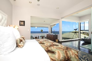 A modern hotel room with a large bed, a view of the ocean, and a telescope on a balcony. - Kapalua Bay Villas | Ocean View 2 BR | Car Incl. w/ 6+ Nights | KBV-24B2 by KBM (Lahaina)