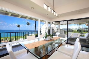 A modern dining area with a glass table, white chairs, and a view of the ocean.