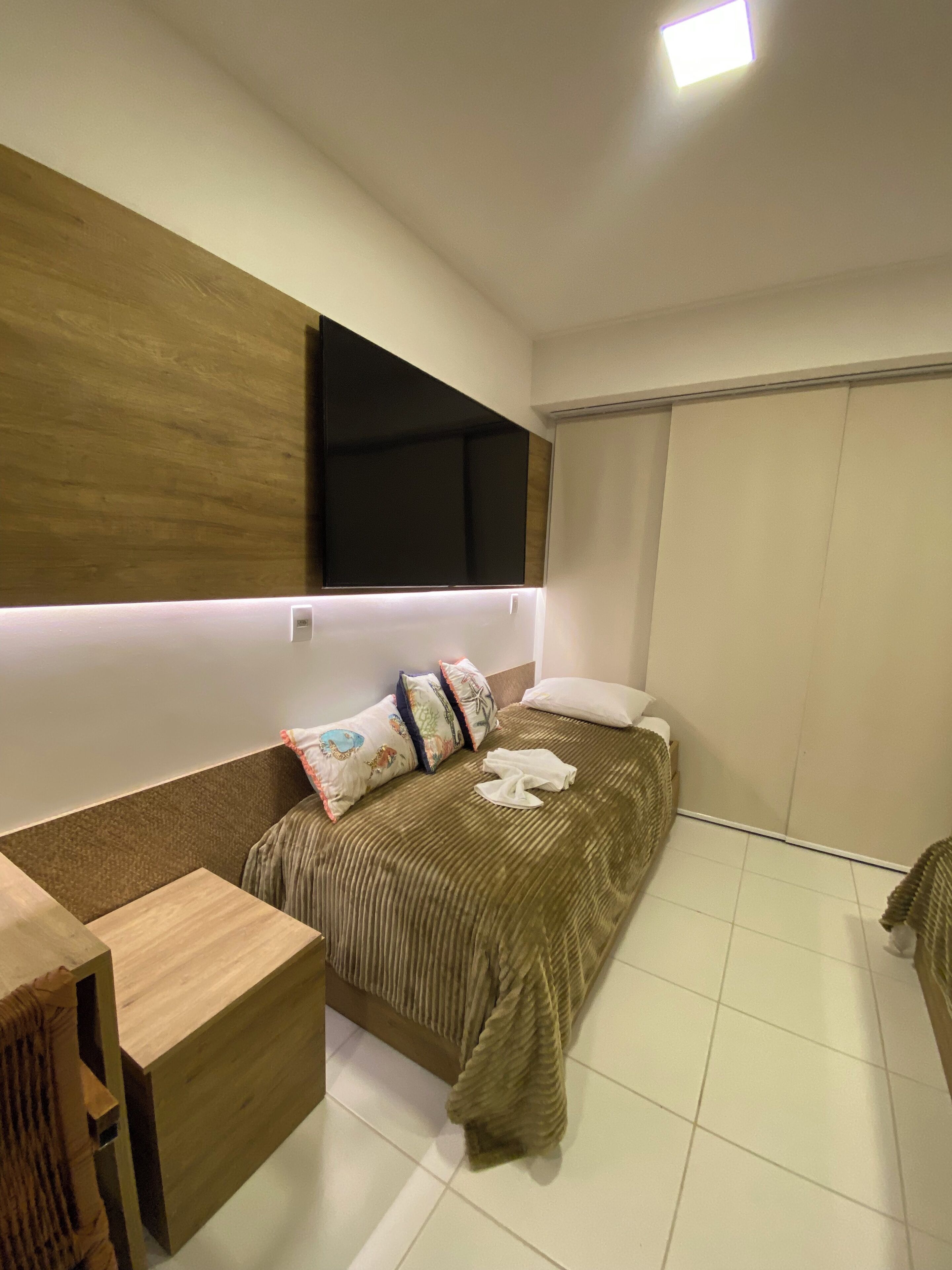 Un dormitorio moderno con cama, mesita de noche y televisión integrada.